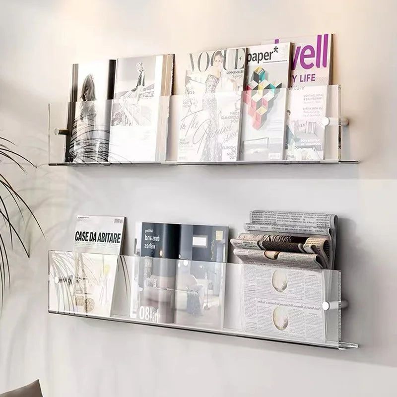 Transparent acrylic Avenue Wall-Mounted Magazine Shelf displaying magazines and newspapers on a white wall.