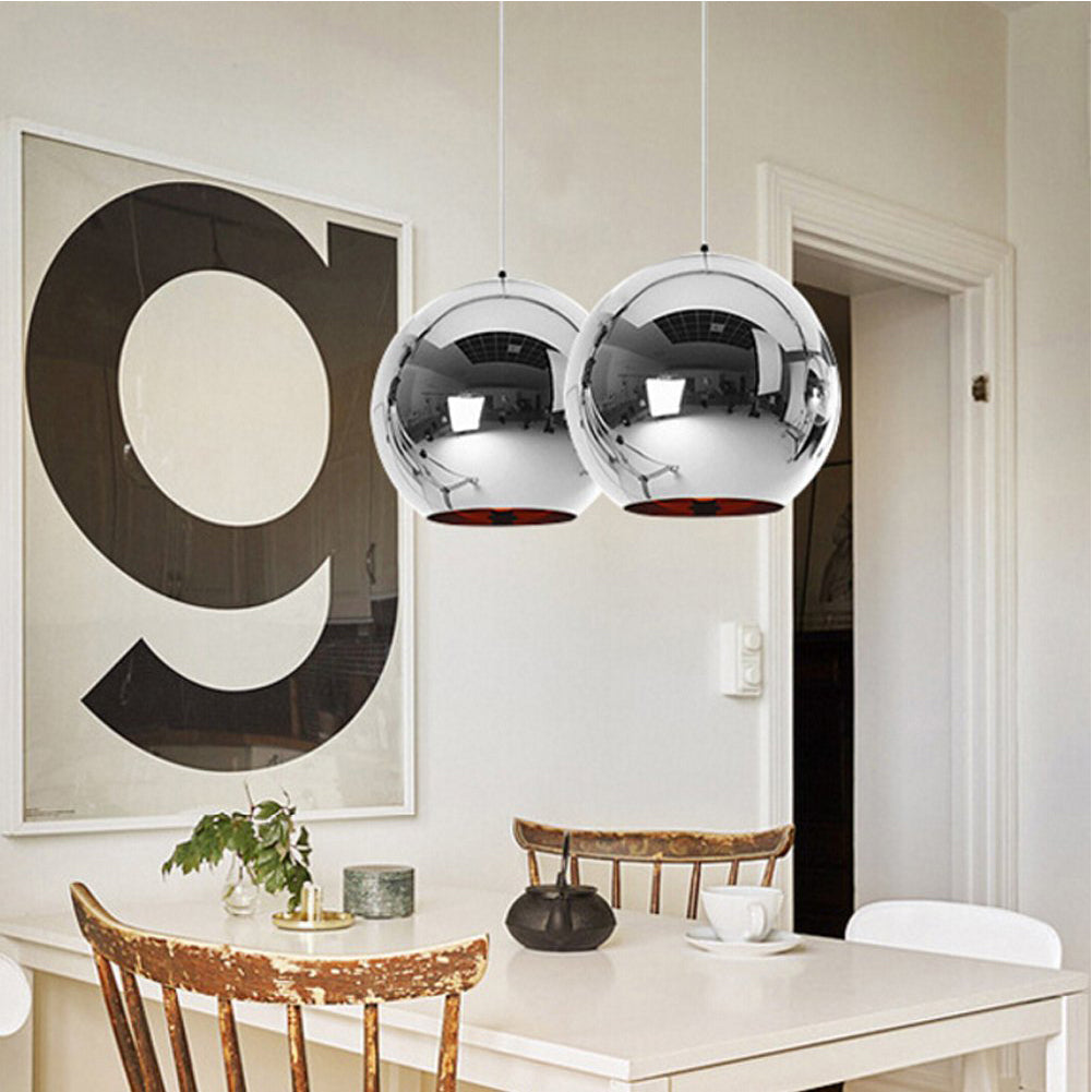 Two chrome spherical Chroma pendant lights hanging over a white dining table with wooden chairs.