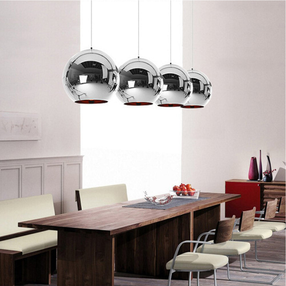 Four chrome spherical pendant lights with orange interiors hang over a wooden dining table.