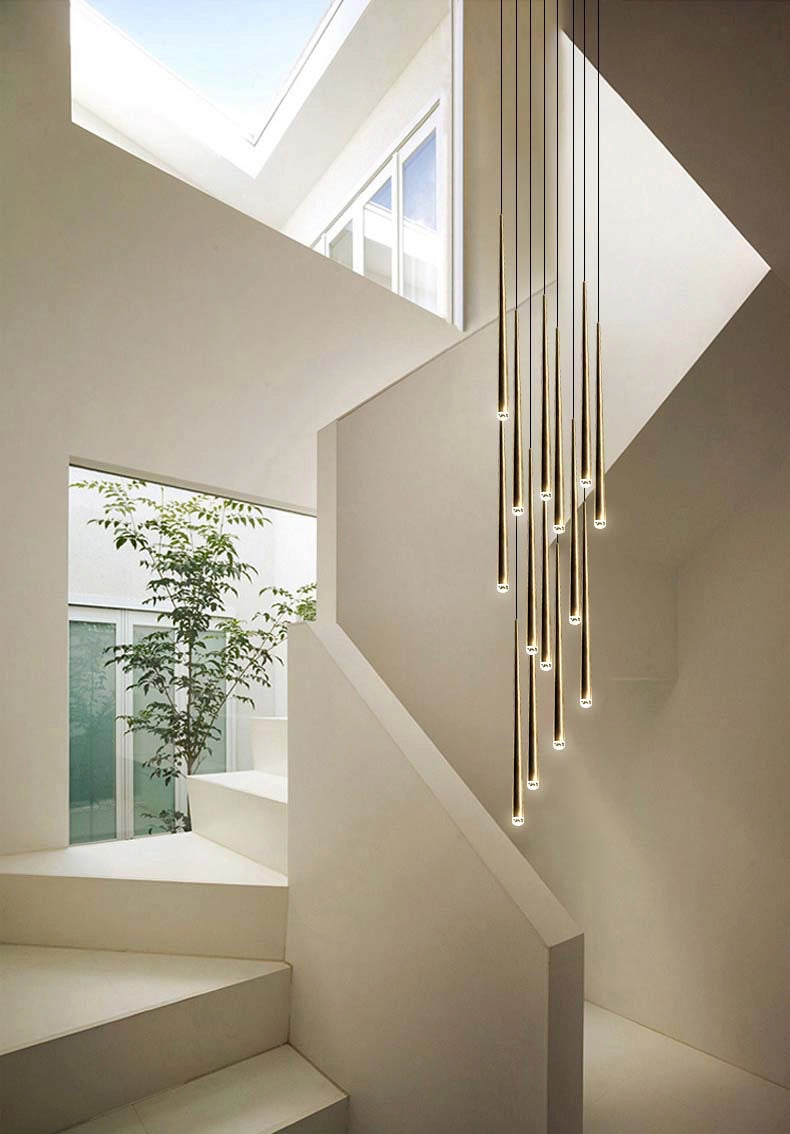 Evora gold pendant chandelier with multiple slender, cylindrical lights hanging in a modern white stairwell.