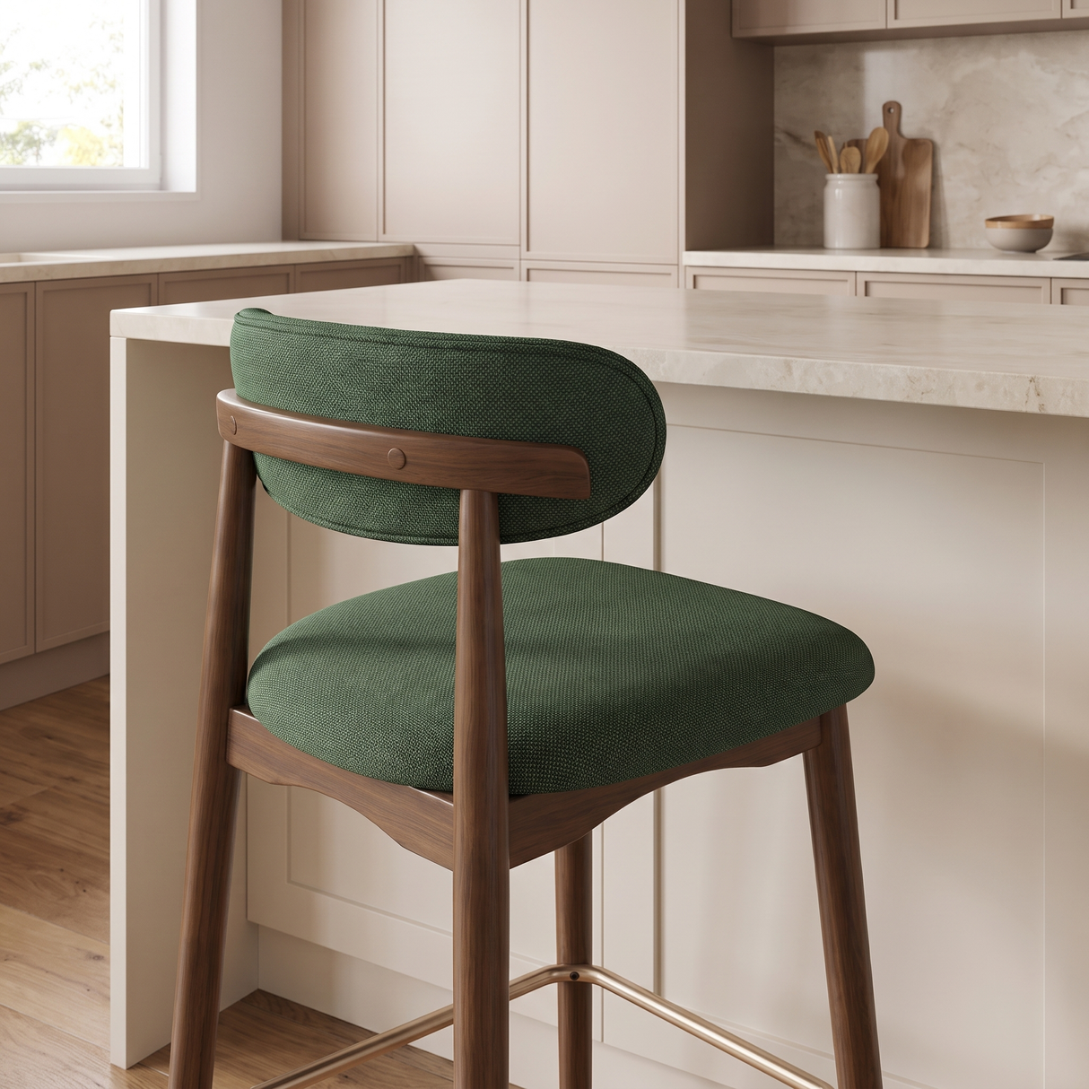 A modern bar stool with a green textured fabric seat and backrest, supported by a curved wooden frame with gold-toned metal legs, set in a bright, contemporary kitchen.