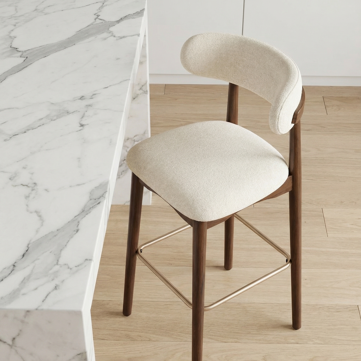 Norden Bar Stool with curved cream upholstered seat and back, dark wood frame, and brass footrest.