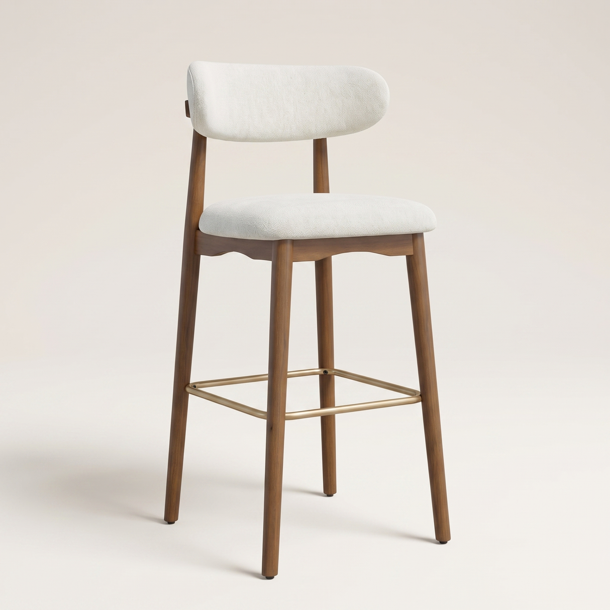 A modern bar stool with a light beige upholstered seat and curved backrest, supported by a medium brown wooden frame with a gold metal footrest, set against a solid light beige background.