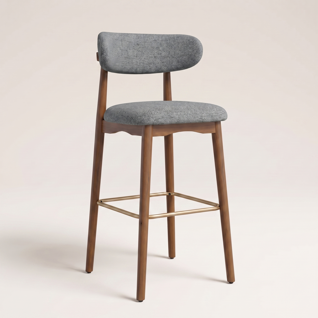 A modern bar stool with a curved gray upholstered backrest and seat, supported by a medium brown wooden frame with a gold metal footrest, set against a solid light beige background.