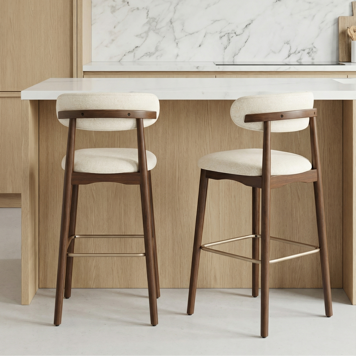 Norden Bar Stool in ivory fabric with a dark wood frame and brass footrest, shown at a kitchen island.
