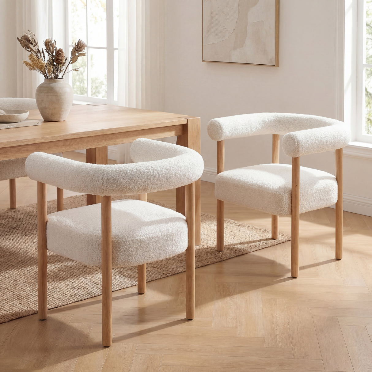 Sarlo Dining Chair in white boucle with light wood legs and curved backrest, shown in a dining room.