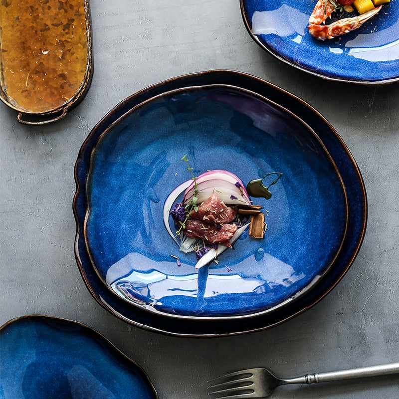 Atlas Dinner Plate, deep blue ceramic with irregular dark rim, holding a small appetizer.