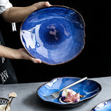 Atlas Dinner Plate: Hand holding a deep blue ceramic dinner plate with an irregular rim. Another plate below holds food.
