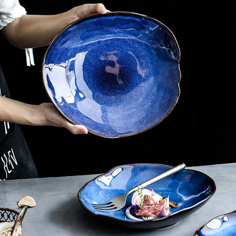 Atlas Dinner Plate: Hand holding a deep blue ceramic dinner plate with an irregular rim. Another plate below holds food.