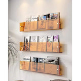 Three amber acrylic wall-mounted magazine shelves holding various magazines on a white wall.