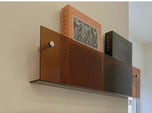 Avenue wall-mounted magazine shelf in tea-colored acrylic, 30cm, holding books on a beige wall.