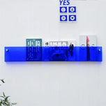 Blue acrylic Avenue Wall-Mounted Magazine Shelf, 30cm, holding books and magazines on a white wall.