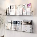 Transparent acrylic Avenue Wall-Mounted Magazine Shelf displaying magazines and newspapers on a white wall.