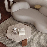 Borra Coffee Table: Hexagonal travertine top with dark wood base, on a textured rug next to a curved sofa.