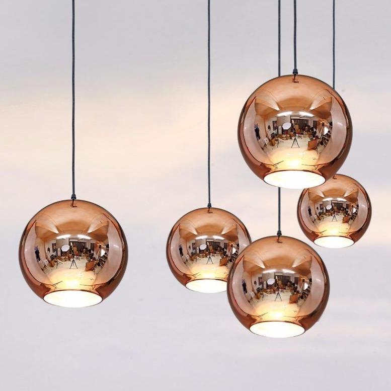 Five round copper glass Chroma pendant lights with reflective surfaces hang from black cords.