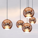 Five round copper glass Chroma pendant lights with reflective surfaces hang from black cords.