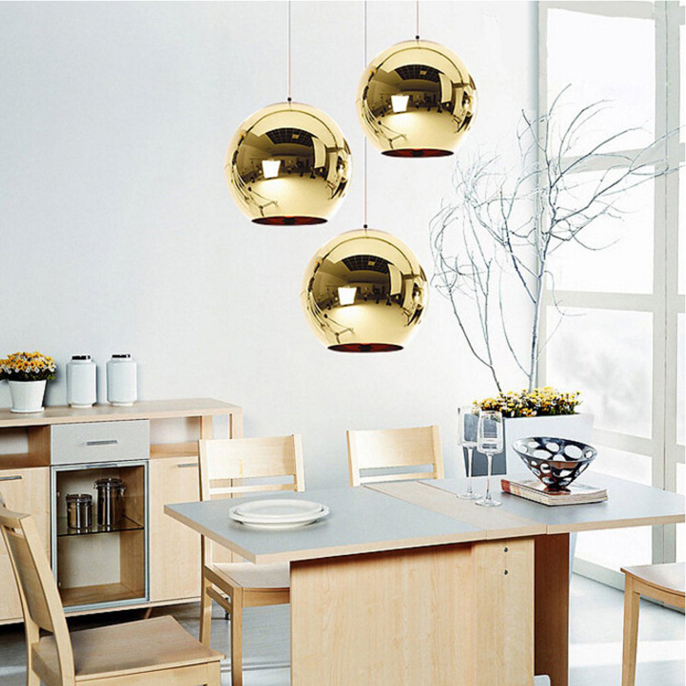 Three round, reflective gold Chroma pendant lights hang above a dining table.