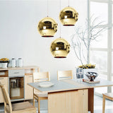 Three round, reflective gold Chroma pendant lights hang above a dining table.