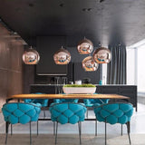 Five copper Chroma pendant lights hang above a long wooden dining table with blue upholstered chairs.