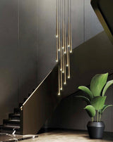 Evora pendant chandelier with multiple long, slender gold-toned lights hanging over a dark staircase.