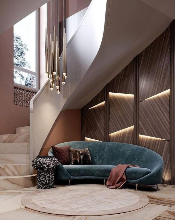 Evora pendant chandelier with multiple gold-toned tubes and small lights, hanging over a curved blue velvet sofa.