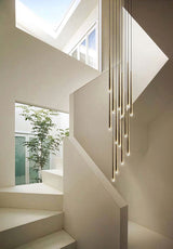Evora gold pendant chandelier with multiple slender, cylindrical lights hanging in a modern white stairwell.