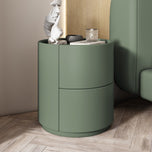 Mira Bedside Table in avocado green with two drawers and a round top, on a light wood floor.