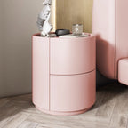 Mira Bedside Table, a round pink nightstand with two drawers, on a light wood floor.