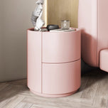 Mira Bedside Table, a round pink nightstand with two drawers, on a light wood floor.