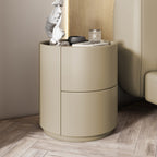 Mira Bedside Table in khaki, a round nightstand with two curved drawers, next to a bed.