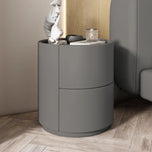 Mira Bedside Table in dark gray with two curved drawers, shown next to a bed.