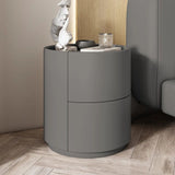 Mira Bedside Table in dark gray with two curved drawers, shown next to a bed.