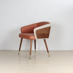 Modenal Dining Chair in orange leather with beige trim, wood paneling, and gold-capped tapered legs.