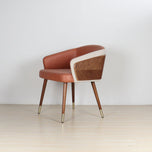 Modenal Dining Chair in orange leather with beige trim, wood paneling, and gold-capped tapered legs.