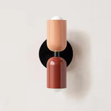 Mura Wall Light, a modern wall sconce with two cylindrical shades in terracotta and burnt orange, on a black base.