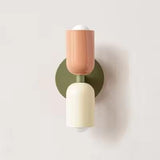 Mura Wall Light, a modern wall sconce with a peach top shade and cream bottom shade on an olive green base.