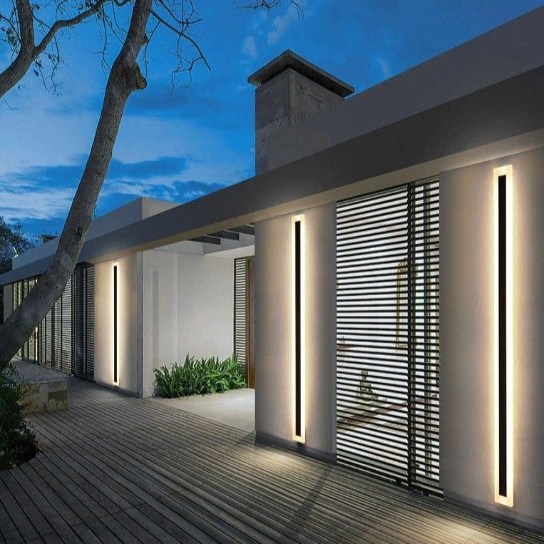 Spire Outdoor Wall Light, a modern black vertical wall sconce illuminating a contemporary building exterior.