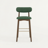 Norden Bar Stool with dark green upholstered seat and back, walnut wood frame, and brass footrest.