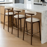 Three Norden Bar Stools with dark wood frames, light fabric seats, and curved backs at a kitchen island.