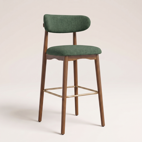 A modern bar stool with a green upholstered seat and curved backrest, supported by a medium brown wooden frame with a gold metal footrest, set against a plain light beige background.