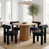 Rogolo Dining Chair. Four black velvet dining chairs with cylindrical legs and backs around a round fluted wood table.