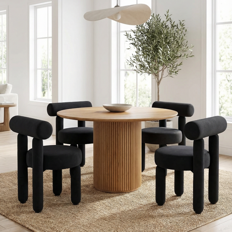 Rogolo Dining Chair. Four black velvet dining chairs with cylindrical legs and backs around a round fluted wood table.