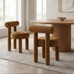 Rogolo dining chair in rust velvet with rounded back and legs, next to a matching chair and wood table.