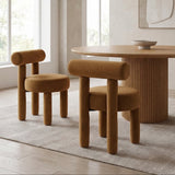 Rogolo dining chair in rust velvet with rounded back and legs, next to a matching chair and wood table.