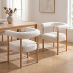 Sarlo Dining Chair in white boucle with light wood legs and curved backrest, shown in a dining room.